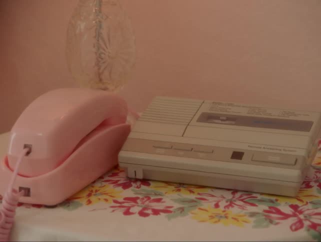 A pink telephone on a desk next to an answering machine