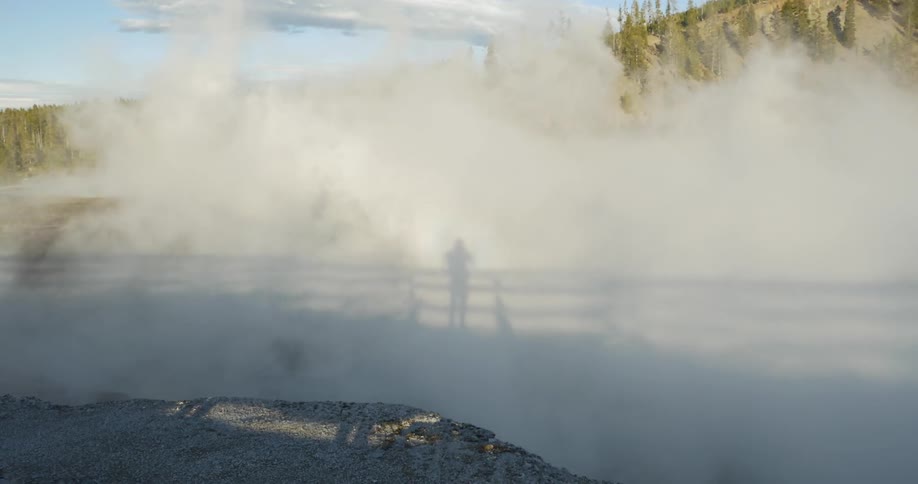 The shadow of a person standing by a fence through a cloud of smoke in a mountainous area