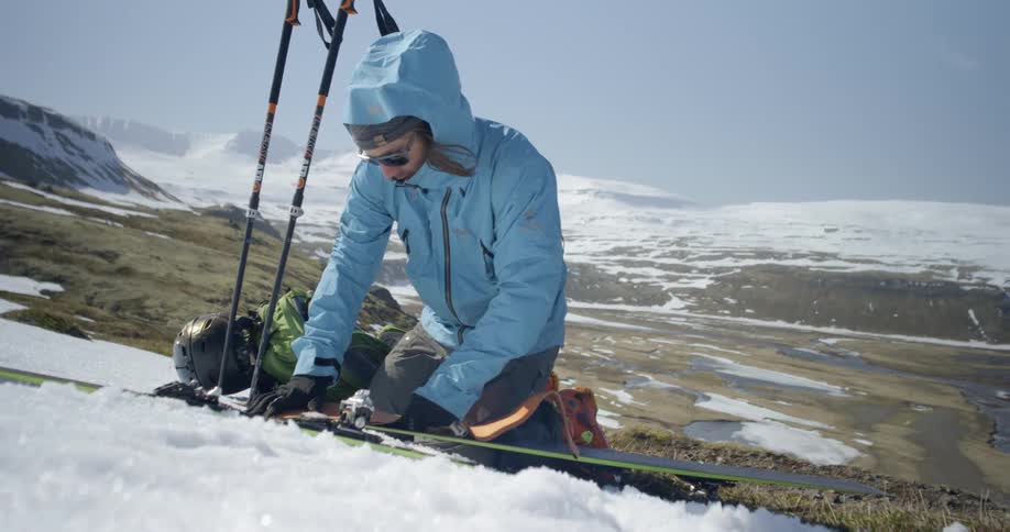 A man applies skins to skis while kneeling in snow on beautiful blue sky day