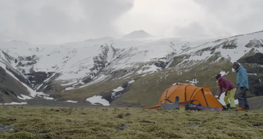 A man and woman stand next to a tent in snowy mountains