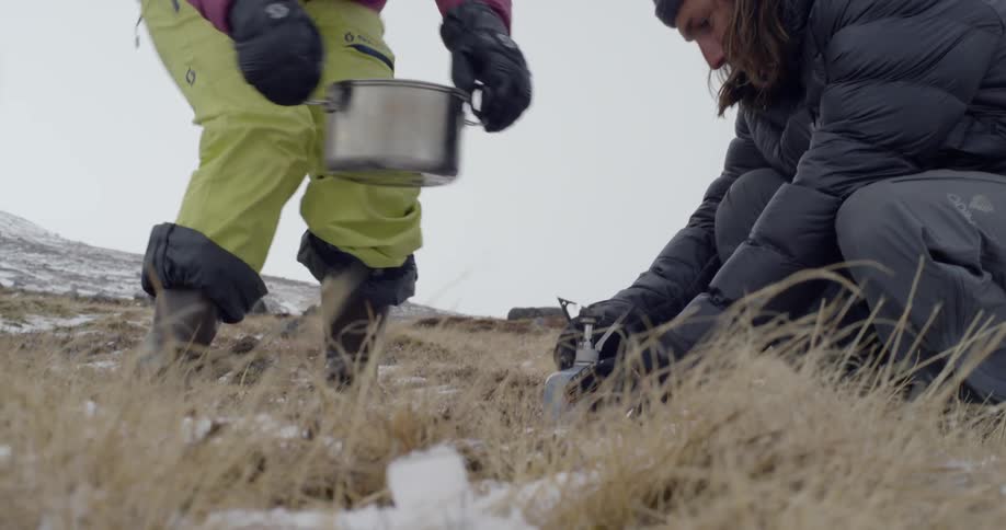 A man and woman cook while camping in the winter