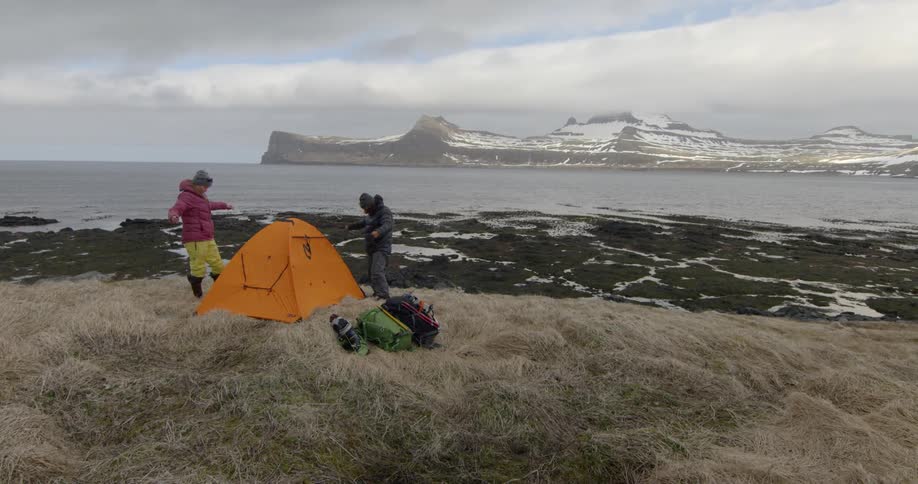 A man and woman stand next to a tent in snowy mountains