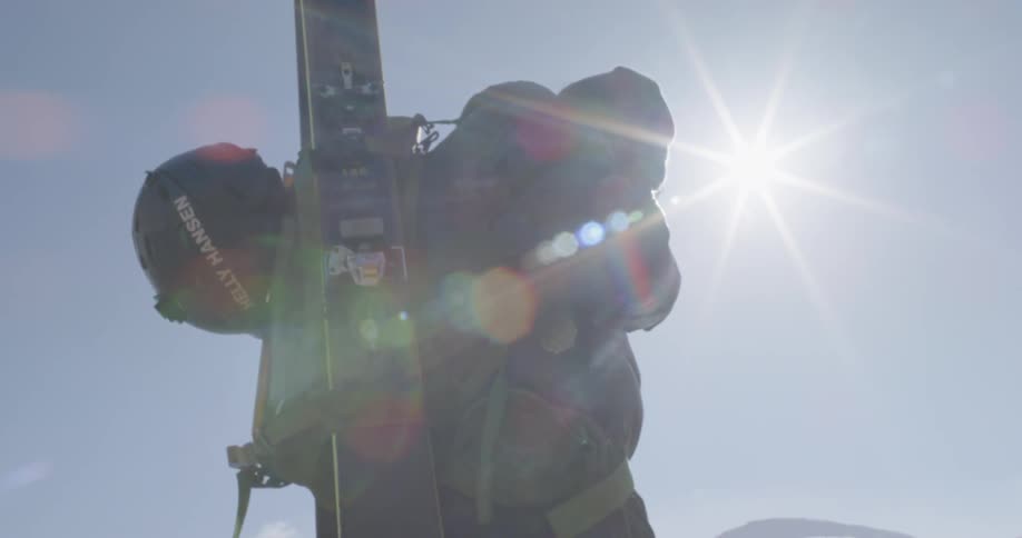 Man straps on backpack with skis attached outside on sunny day