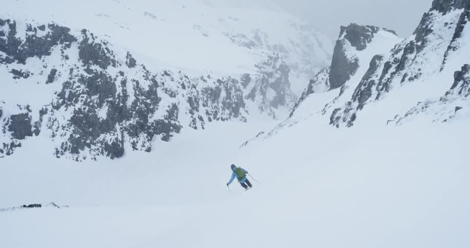 A professional skier skis down a snowy mountainside during storm into chute