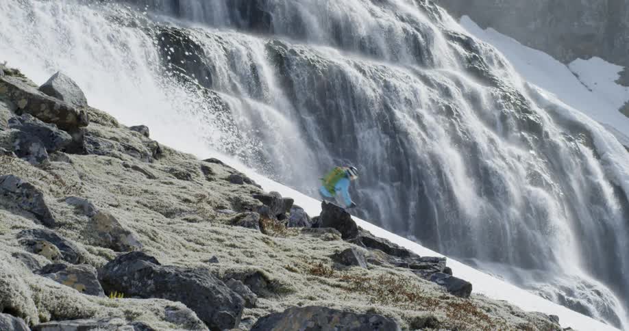 A skier skis in front of massive waterfall in slow motion