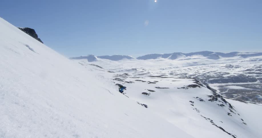 Person skiing down a steep snow covered mountain on sunny day