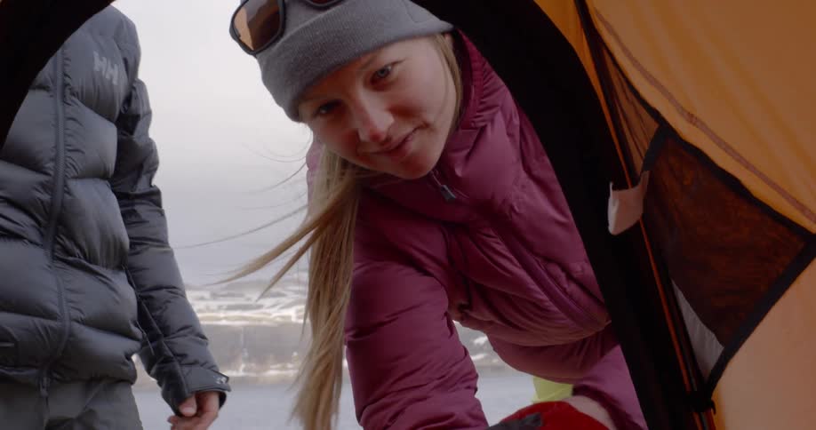 Woman tosses sleeping bag into tent near snowy mountains