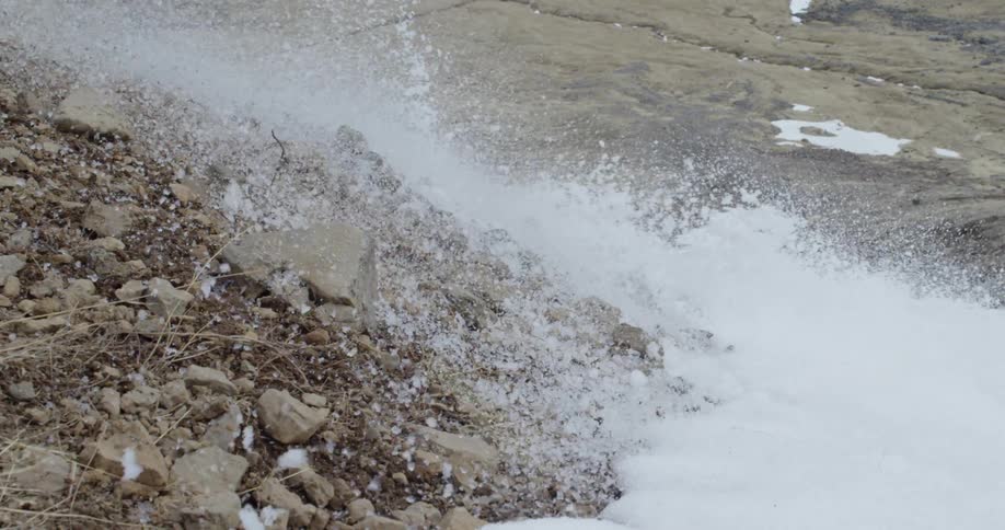 Snow crashes onto a rocky cliff side