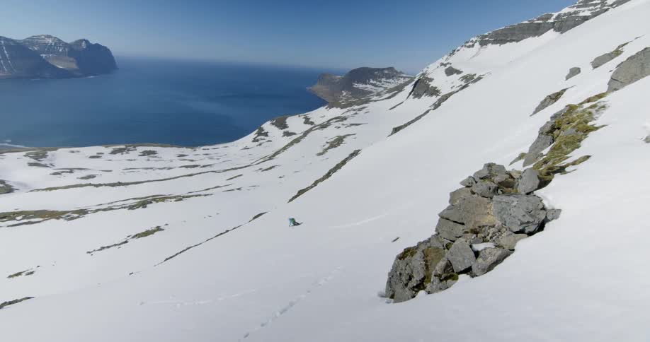 A man skis down a snowy mountainside towards the ocean