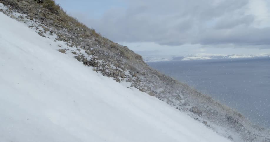 A man making a turn on steep slope throws snow onto rocks