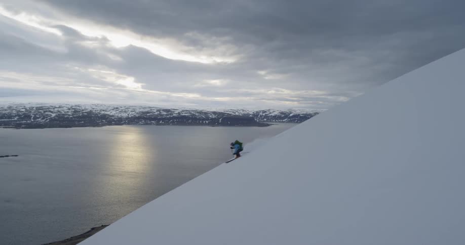 A man skis down the snow at sunset with ocean below