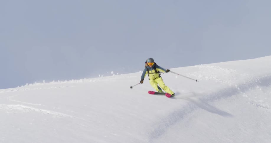 A female skiing down a snow covered mountain slope on sunny day