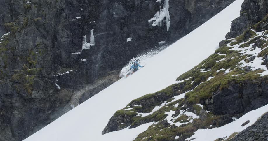 Man skiing down a steep slope as it's snowing with moss and waterfalls