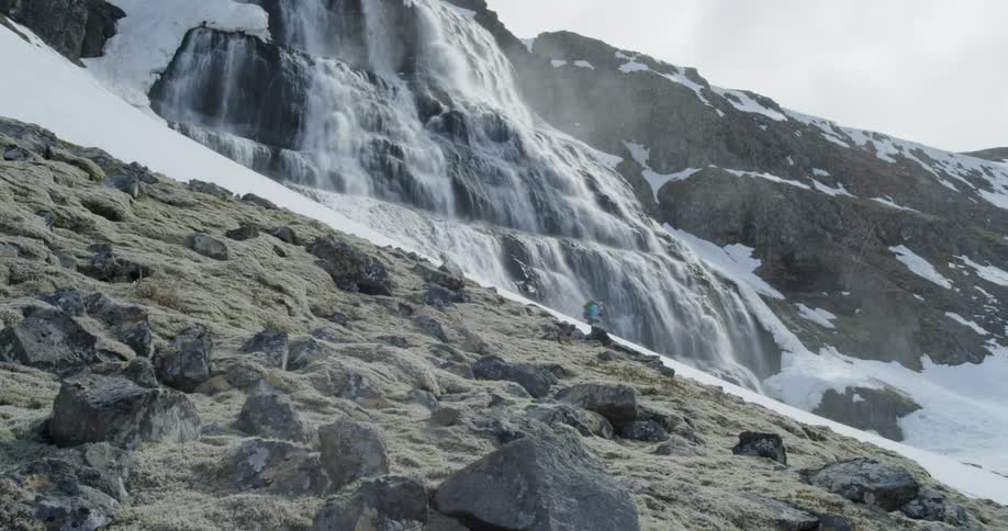 A person skis down a slope next to a large waterfall