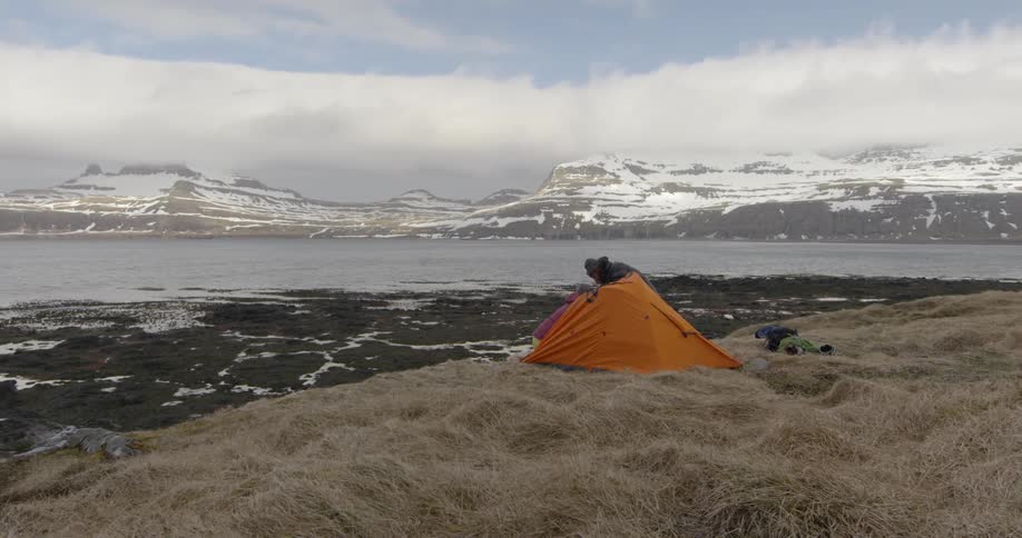 A couple setting up their tent on a cold windy and cloudy day