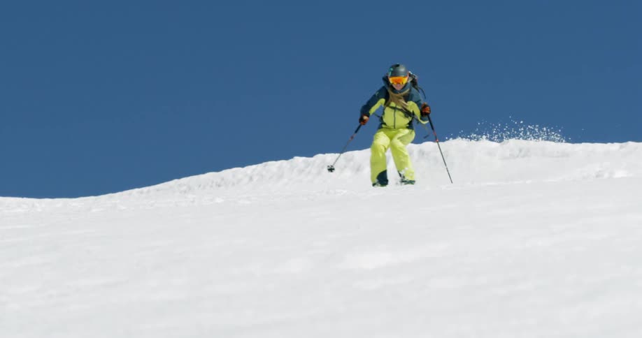 Woman smiles skiing down a snow covered mountain slope on sunny day
