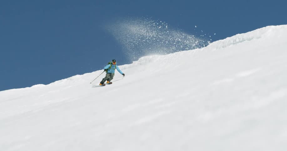 A man in blue jacket skiing down a snow covered mountain on sunny day