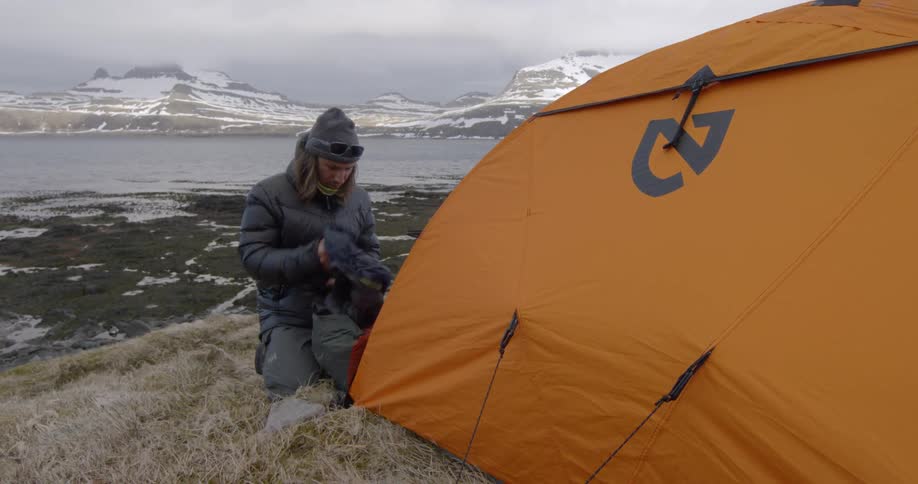 A man kneels next to a tent and pulls out a sleeping bag