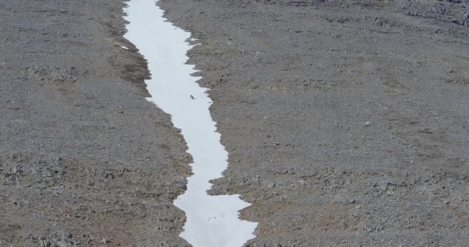 A man skis down a narrow strip of snow on a mountain
