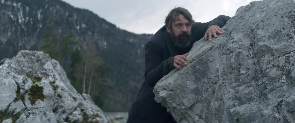 A man struggles to climb over rocks on the shore
