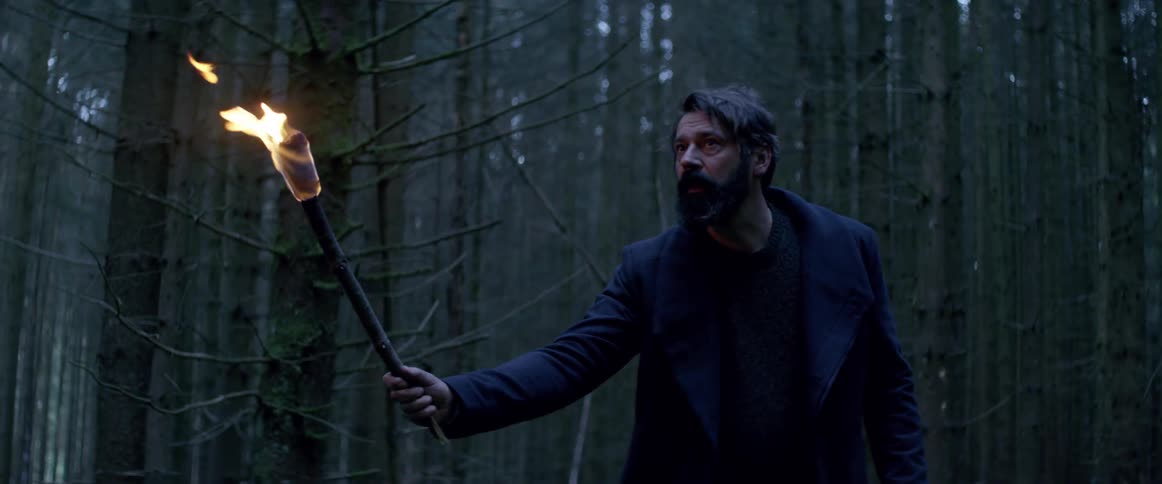 A man in a forest is walking cautiously and brandishing a torch