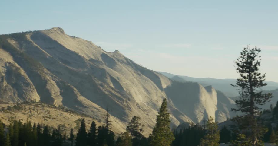 A view of pine trees, mountains and people walking along a trail