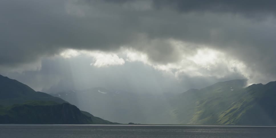 The sun is casting rays onto coastal mountains as a storm passes during the day