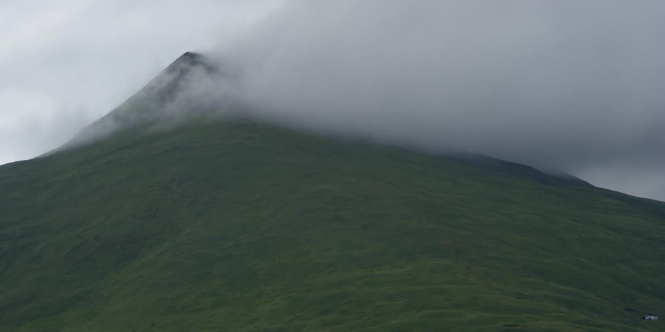 Clouds pass a grassy mountain peak