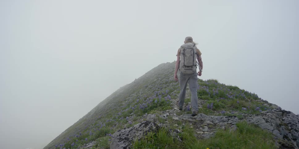 A man is walking up to the peak of a mountain