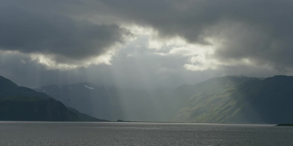 Sunlight is peeking through clouds and shining on the sea