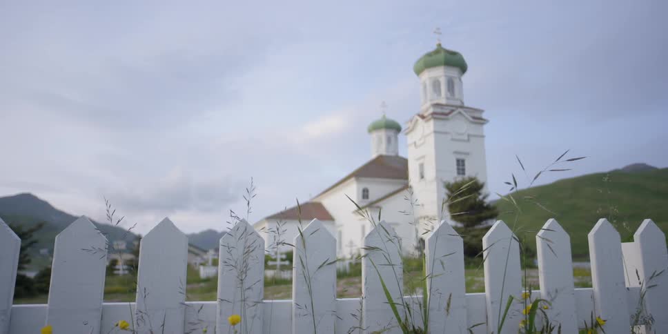 An eagle flies over a fence outside a churchyard on a cloudy day
