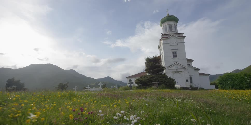 A church and cemetery stand in a field of grass and wildflowers