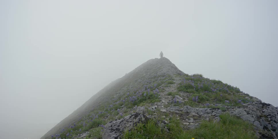 Fog drifts over a mountain ridge line as a man hikes up it