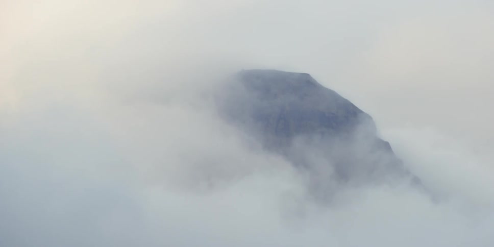 Fog is drifting across a mountain top during the day
