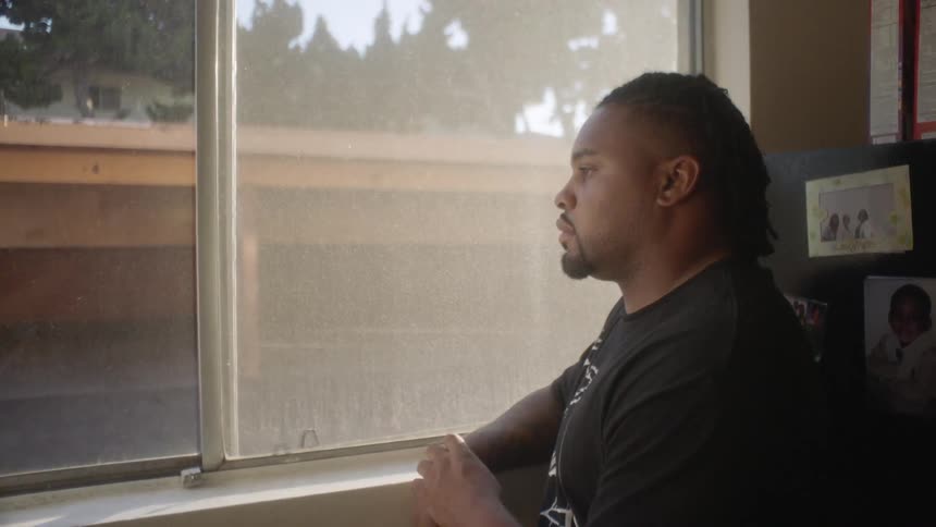A man is sitting deep in thought as he stares out a window during the day