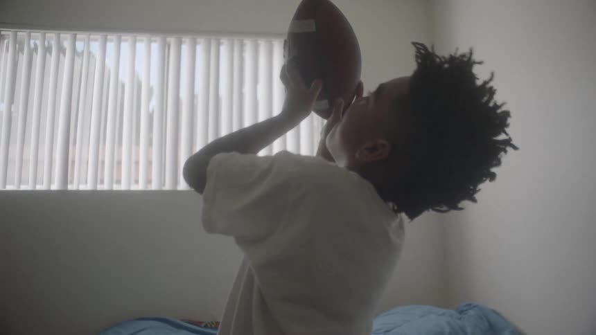 Boy sits on his bed tossing a football
