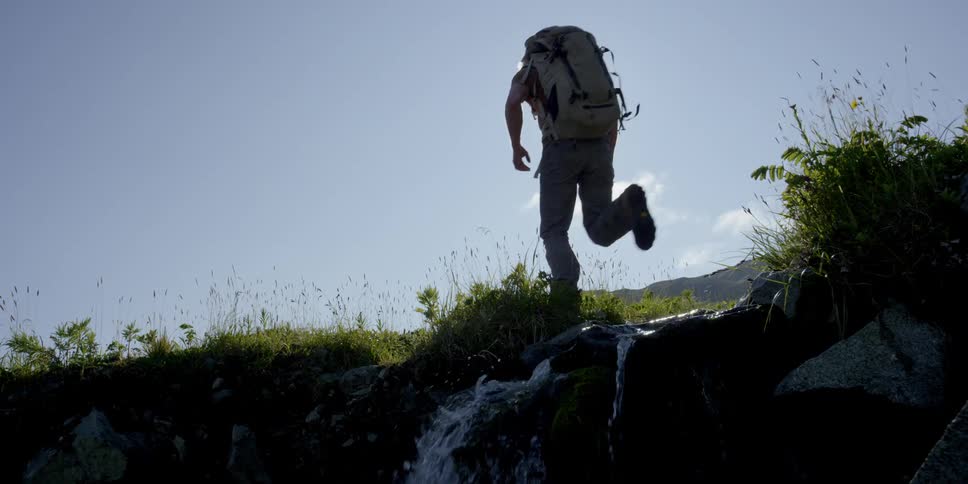 A hiker leaps over a cascading stream on a sunny day
