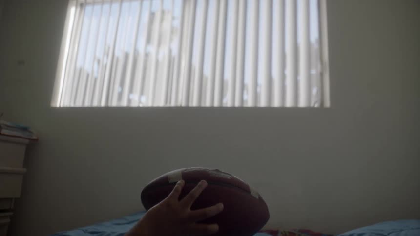 A young boy is lying on his bed and tossing a football during the day