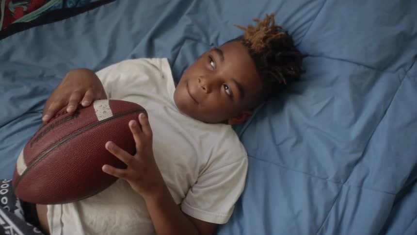 Boy lays on his bed holding a football