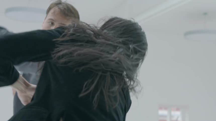 A man and woman are performing a modern dance inside an all white building