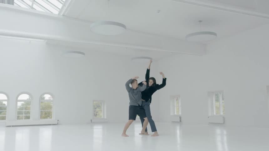 A man and woman are performing a modern dance inside an all white building