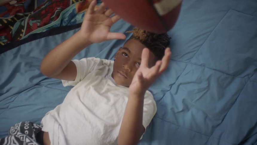 Boy lays on his bed tossing a football