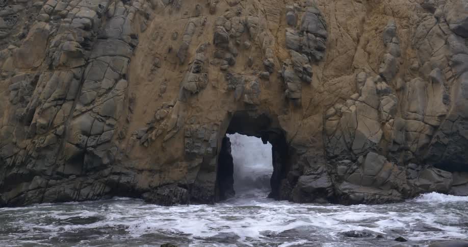 Ocean waves splash through an opening the rock cliff