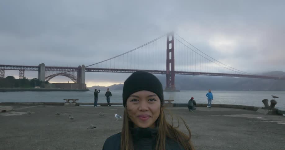 Woman smiling at a lakefront with a bridge in the background