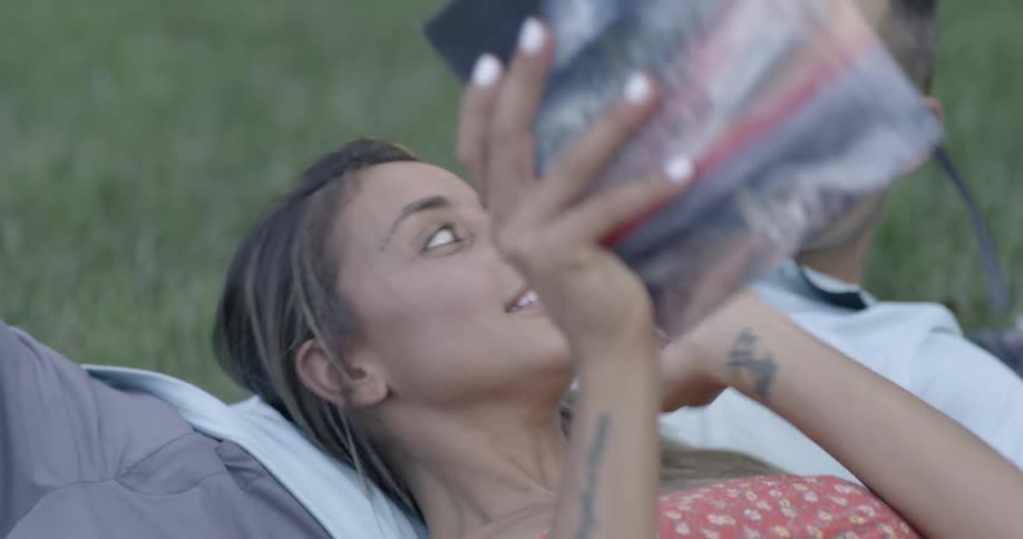 Two people lay on a blanket in the grass and read a book