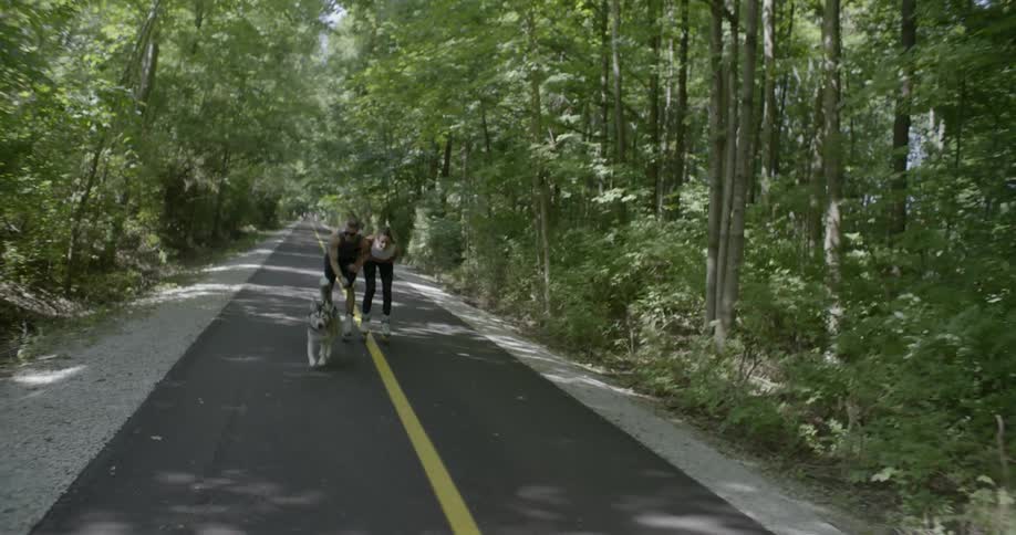 Man and woman rollerskate while walking a dog