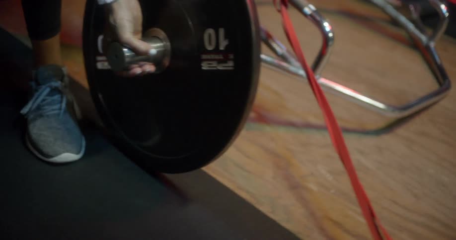 A woman adds a weight to a barbell in a gym