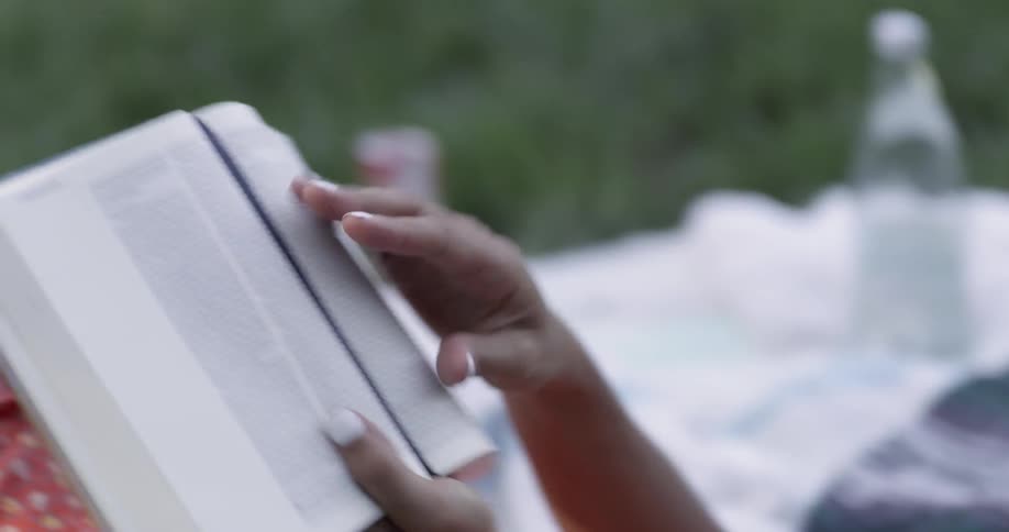 A man and woman are laying in the grass reading a book together
