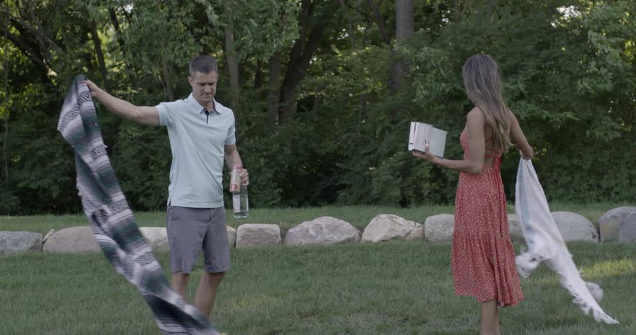 Man and woman pick up blankets from a grassy lawn