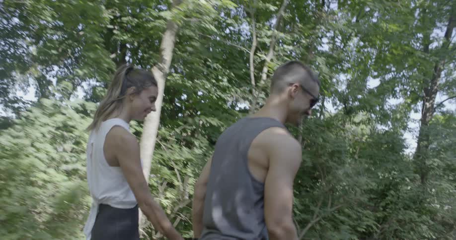 A man and woman are skating down a path in the forest with their dog on a leash